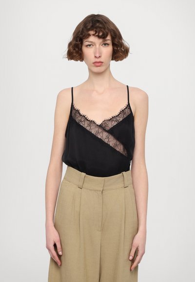 Black camisole featuring lace trim and thin straps, paired with high-waisted beige trousers with pleats and a tailored design.