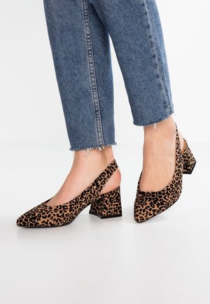 Stopy w niebieskich skróconych jeansach i sandałach slingback na słupku w panterkę na białej podłodze.