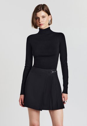 Maglione nero a collo alto abbinato a una gonna plissè nera. La gonna presenta un accento in metallo argentato in vita, creando una silhouette elegante.
