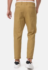Pantalones chinos beige con una textura suave, corte ajustado y puños enrollados. Cuentan con bolsillos traseros y se combinan con zapatillas blancas.