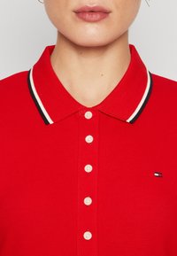 Rode polo shirt met een klassieke kraag, witte knopen aan de voorkant en een contrasterende zwart-wit gestreepte kraagaccent. Klein logo op de borst.