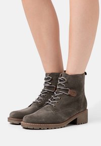 Botines de ante gris con punta redonda, cordones en la parte frontal y tacón de bloque de madera; cuentan con ojales de metal y un acento de cuero marrón.