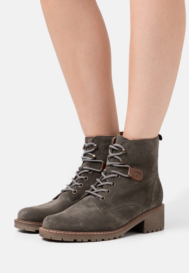 Botines de ante gris con punta redonda, cordones en la parte frontal y tacón de bloque de madera; cuentan con ojales de metal y un acento de cuero marrón.