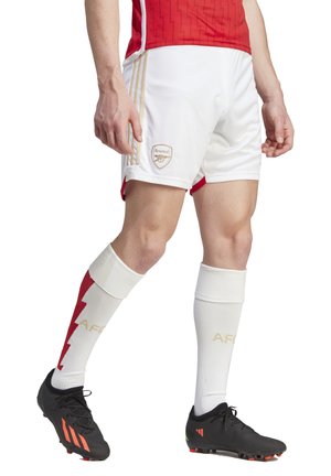 Arsenal football kit featuring a red jersey with zigzag pattern, white shorts, black cleats, and red and white socks with gold accents.