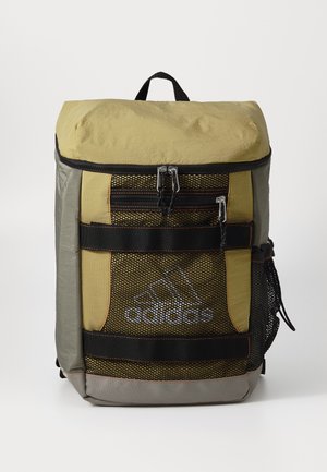 Mochila ligera de color verde oliva y gris con panel de malla, correas negras, cremalleras plateadas y el logo de Adidas en la parte frontal. Forma cuadrada.