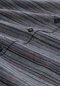 Grau karierte Button-Up-Hemd mit vertikalen Streifen in Rot und Schwarz. Der Stoff ist strukturiert mit kleinen gewebten Mustern und schwarzen Knöpfen.