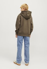 Sudadera con capucha marrón, material suave, corte relajado, combinada con jeans de color azul claro y zapatos casuales con suela marrón y rayas verdes.