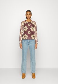 Blusa de manga longa transparente em bordô com padrão floral em creme, combinada com jeans de perna reta azul clara e botas de tornozelo castanhas.