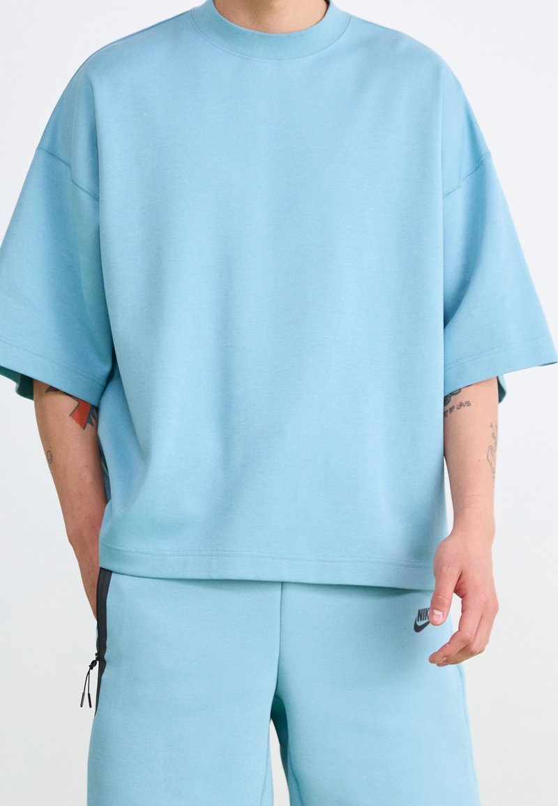 T-shirt oversize bleu clair en tissu lisse avec un col rond et des manches courtes, associé à un short assorti avec des zippers latéraux.