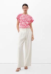 Ein kurzärmliges, blumengemustertes, pinkes Oberteil, kombiniert mit weiten, weißen Hosen, ergibt ein auffälliges, aber minimalistisches Outfit. Glatter Stoff mit lockerer Passform.