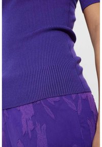 Lila ribbad stickad topp med korta ärmar, kombinerad med lila texturerade byxor med en präglad blommönsterdesign. Mjuk tyg och figurnära stil.