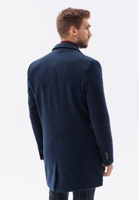 Navy ullblandad kappa med en enda slits, spetsig krage och knapppdetaljer på ärmarna. Slät textur, skräddarsydd passform och minimalistisk design.