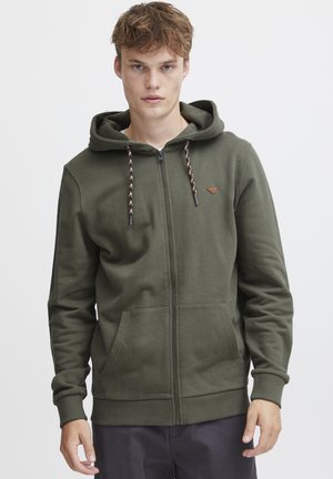 Sudadera con cremallera de color verde oliva, hecha de tejido suave, que cuenta con una capucha con cordón, bolsillos frontales y un pequeño detalle de logo en el pecho.