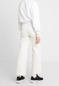 Pantalons larges taille haute blancs avec poches avant, accompagnés d'un sweatshirt blanc et de chaussures de sport noires. Texture en coton lisse.