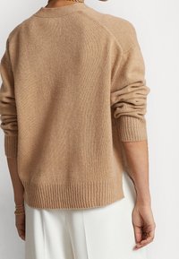 Ljusbeige stickad tröja med rund halsringning, ribbad mudd och nederkant, med en avslappnad passform och uppvikta kanter vid ärmarna.