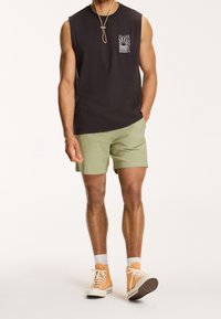 Černé bavlněné tričko bez rukávů s bílým grafickým potiskem, spárované se světle zelenými šortkami. Nosené s oranžovými vysokými teniskami.