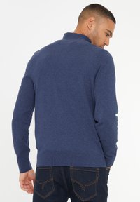 Marineblauer Pullover mit hohem Kragen, gerippten Bündchen und Saum. Hergestellt aus weichem Stoff, bietet eine glatte Textur und eine taillierte Passform.