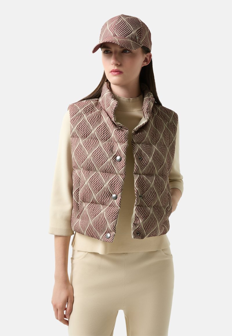 Padded vest z falistym wzorem w czerwono-kremowych odcieniach, z wysokim kołnierzem i zatrzaskami. Pasująca czapka w ten sam wzór dopełnia outfit.