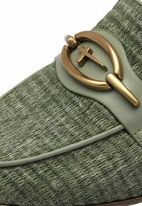 Zelená texturovaná bota s hladkým koženým páskem a výrazným zlatým detailem s přezkou. Design se vyznačuje oválným tvarem s křížovým akcentem.