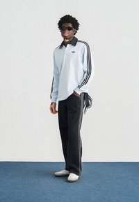 Ανοιχτό γαλάζιο μακρυμάνικο πόλο με μαύρο γιακά και μαύρες ρίγες στα μανίκια, συνδυασμένο με μαύρο παντελόνι φαρδιάς γραμμής και λευκά αθλητικά παπούτσια.