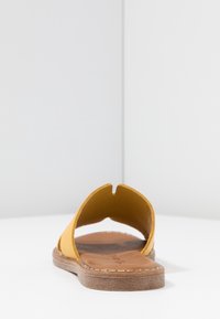 Gul lädersandal med öppen tå-design, brun lädersula och platt gummisula med sömmen detaljer.