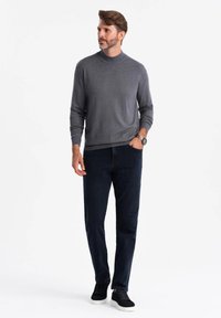 Šedý rolák, tmavě modré kalhoty a černé boty. Svetr má strukturovaný vzor; outfit je neformální a přiléhavý.