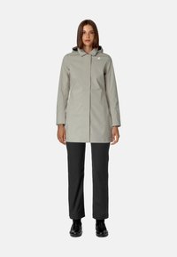 Jasnoszara wodoodporna kurtka przeciwdeszczowa z kapturem, z zamkiem błyskawicznym z przodu i bocznymi kieszeniami, zestawiona z czarnymi spodniami o prostym kroju.