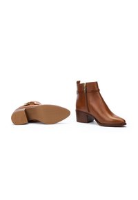 Bottes de cheville en cuir marron avec un bout arrondi, une discrète fermeture éclair sur le côté et un talon bloc moyen. Texture lisse avec un design minimaliste.