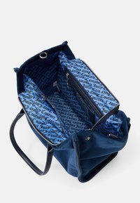 Kovinsko modra suknjana torba iz umetnega usnja z črnimi usnjenimi ročaji. Notranjost ima modro tekstilno oblogo s ponovljenim besedilom "Juicy Couture" v črni barvi.
