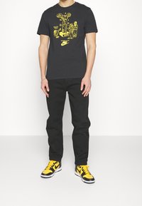 Černé tričko s žlutým grafickým potiskem, kombinované s černými kalhotami a žluto-černými teniskami. Jednoduchý kulatý výstřih.