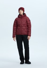 Puchowa bordowa kurtka z zamkiem z przodu, kapturem i pikowanym wzorem. Czarne spodnie i ciemne botki. Prosta, funkcjonalna odzież na świeżym powietrzu.