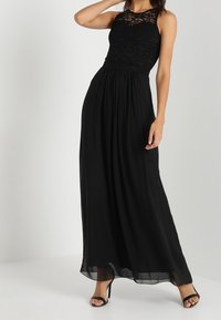 Svart maxiklänning med spetsliv, ärmlös design och flytande chiffongkjol. Inkluderar en figurnära midja och subtila genomskinliga lager.