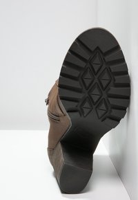 Brązowy botek za kostkę z teksturowaną zamszową cholewką, bocznym zamkiem błyskawicznym oraz czarną gumową podeszwą z wielokierunkowym wzorem bieżnika.