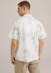 Rövidujjú fehér ing szürke paisley mintával, gombolós gallérral és laza szabással. Az anyag úgy tűnik, hogy könnyű és sima tapintású.