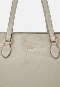 Sac cabas en cuir verni gris clair avec motifs floraux embossés et motifs en forme de "J". Doté de ferrures dorées et de deux poignées solides.
