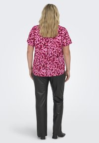 Top a maniche corte con un motivo astratto rosa e bordeaux, abbinato a pantaloni neri in ecopelle. Presenta un design fluido e una vestibilità rilassata.