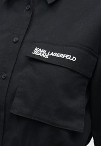 Čierna košeľa na zapínanie s veľkým vreckom na prsiach, na ktorom je bielym vyšívaným logom "KARL LAGERFELD JEANS".