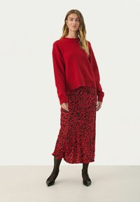 Red knitted sweater paired with a black and red leopard print midi skirt, worn with black heels. Model stands against a white background.