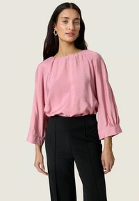 Blusa di seta rosa con una vestibilità ampia, scollatura ampia e maniche a tre quarti, abbinata a pantaloni neri a vita alta. Tessuto liscio.