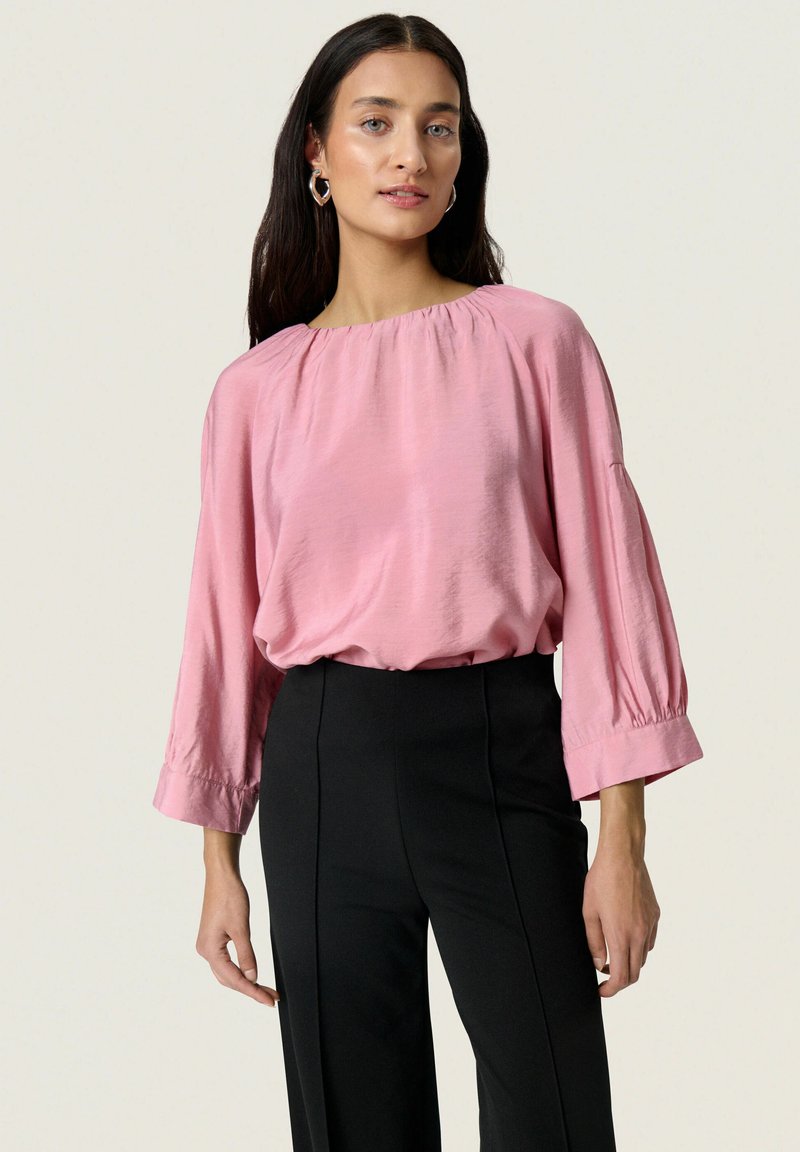 Blusa di seta rosa con una vestibilità ampia, scollatura ampia e maniche a tre quarti, abbinata a pantaloni neri a vita alta. Tessuto liscio.