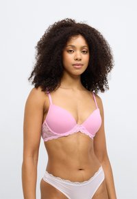 Różowy stanik wyściełany koronką, z regulowanymi ramiączkami i gładką teksturą. W zestawie z białymi majtkami z koronkowym wykończeniem.