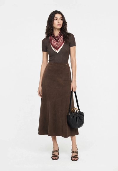 Femme portant un haut marron côtelé à manches courtes, une jupe midi en suède marron, une écharpe rouge à motifs, des sandales noires et tenant un sac à main noir.