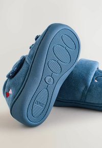 Blå stofslippers med en blød tekstur, prydet med broderede hjerter og en gummisål med skridsikre mønstre. Størrelsesmærket er synligt på sålen.