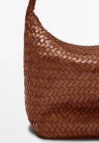 Braune geflochtene Lederhandtasche mit einer geschwungenen Form und einer strukturierten Oberfläche. Verfügt über einen stabilen Tragegurt und ein markantes, kunstvolles Geflechtmuster.