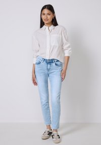 Biała koszula z guzikami i kieszonką, zestawiona z jasnoniebieskimi skinny jeansami. Obuwie to jasnoszare sneakersy z czarnymi akcentami.