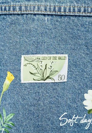 Tkanina dżinsowa z naszywką "Konwalia majowa", kwiatową haftem w żółtym i białym kolorze oraz białym kursywnym napisem "Miękkie dni."