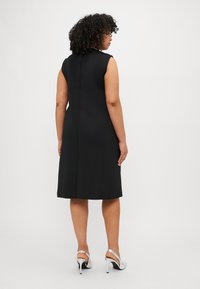 Μαύρο αμάνικο φόρεμα με ίσια γραμμή, λείο υλικό και μήκος μέχρι το γόνατο. Φορεμένο με ασημένια ψηλοτάκουνα παπούτσια.