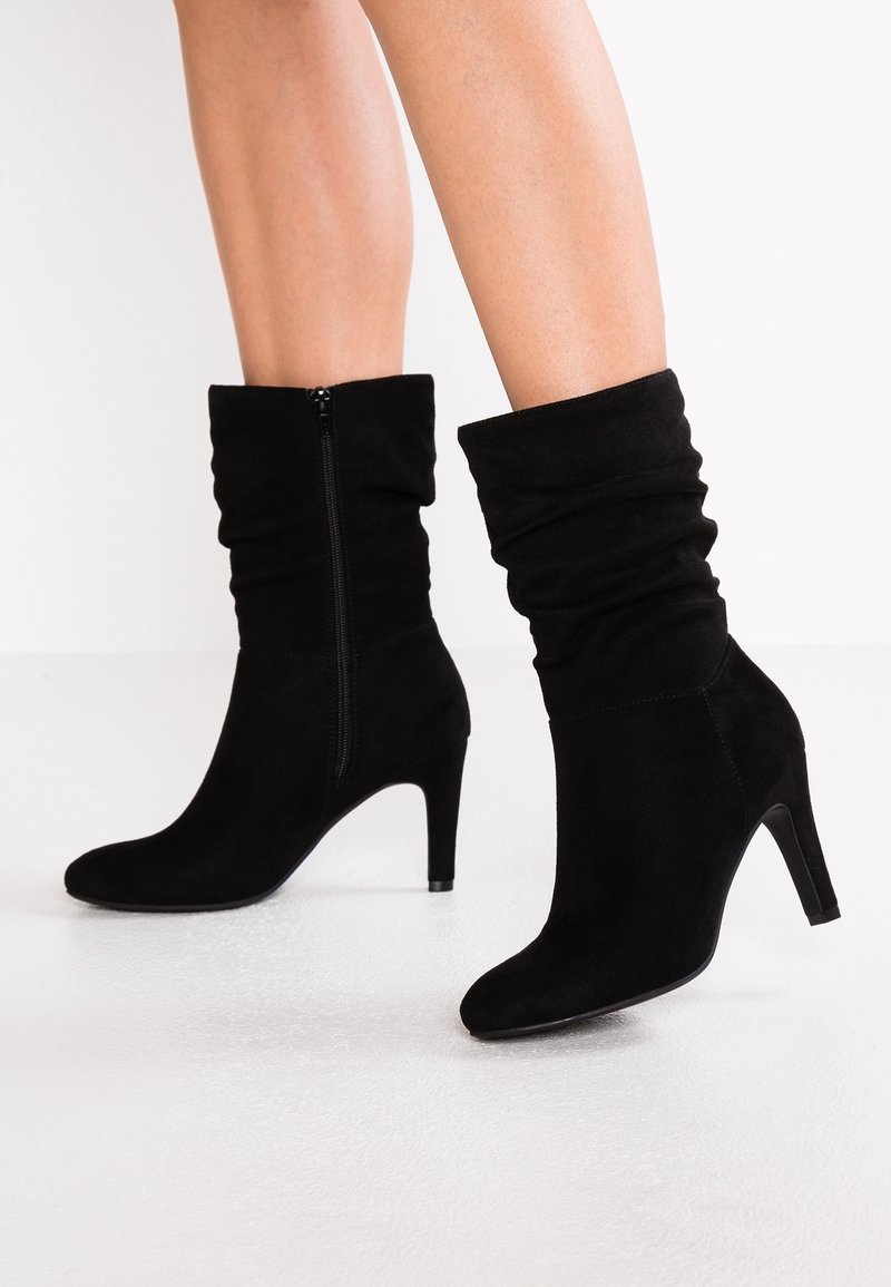 Bottes de cheville en daim noir avec un design froncé, talon haut et fermeture éclair latérale, présentant une texture lisse et un bout arrondi.