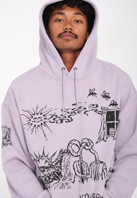 Haut à capuche violet clair avec des graphismes noirs représentant un soleil, des silhouettes et une fenêtre. Capuche avec cordon de serrage et détail de poche avant.