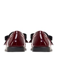 Chaussures en cuir verni marron avec une finition brillante, ornées d'un nœud noir et d'une semelle basse noire, vues de dos.
